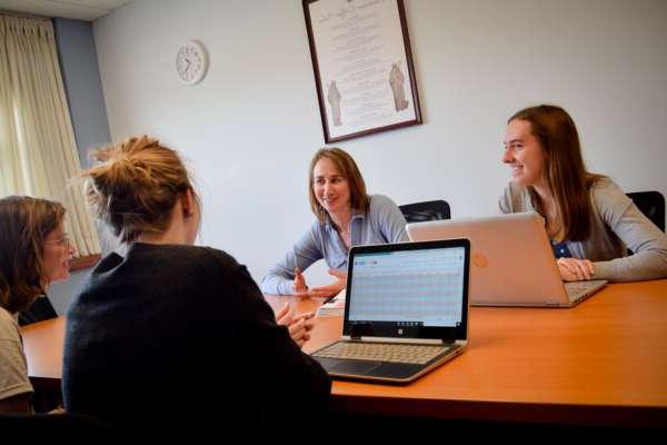 four students discussing at a table with laptops